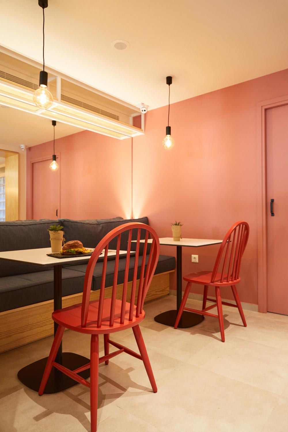 Brunch shop interior, view of table arrangement with build in sofa, red chairs and a big mirror.